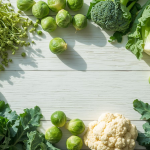 Fresh broccoli sprouts, kale, Brussels sprouts, and cauliflower on a light wooden table, showcasing natural food sources of sulforaphane, a powerful superfood compound.